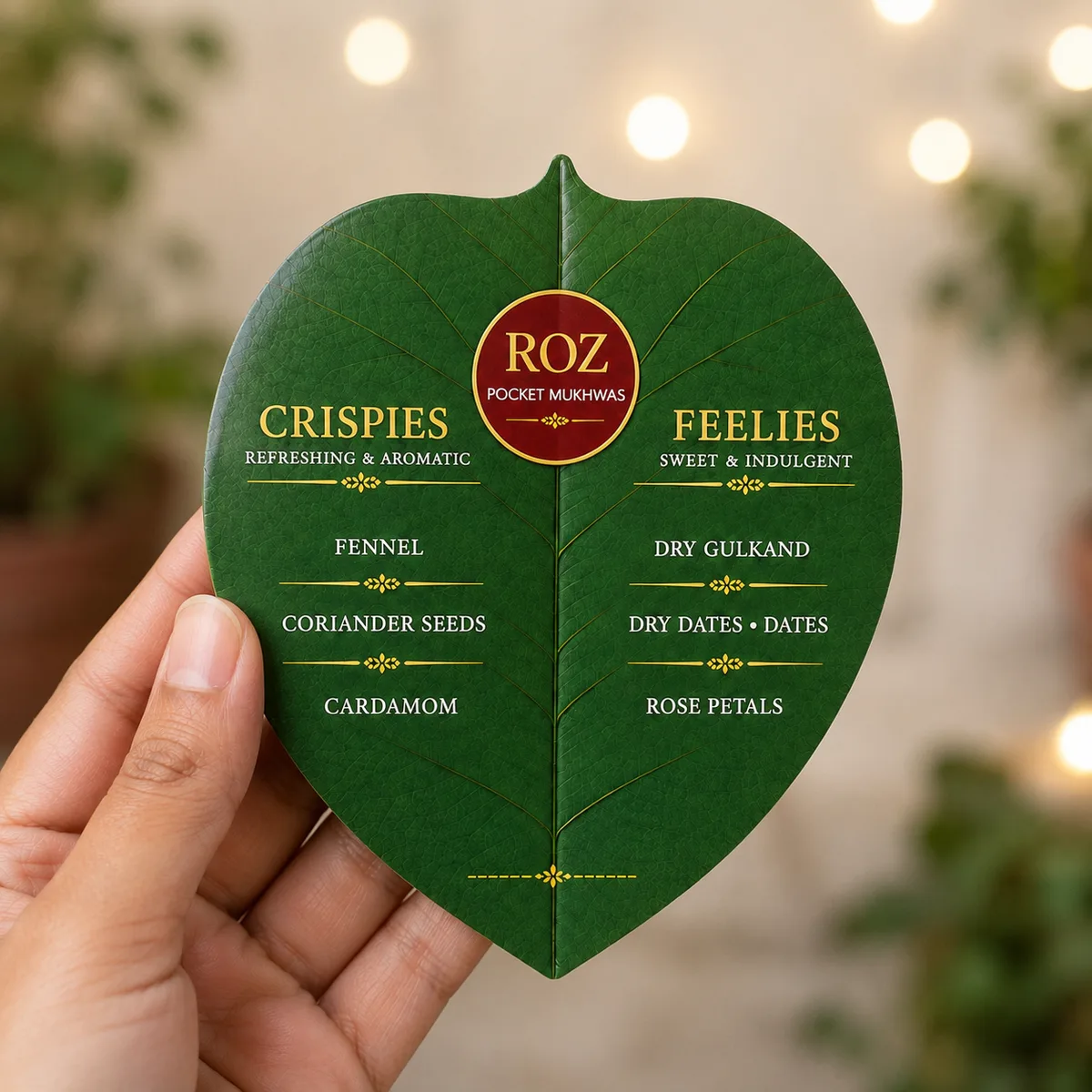 A ROZ mukhwas leaf pack held up, warm lights out of focus behind it